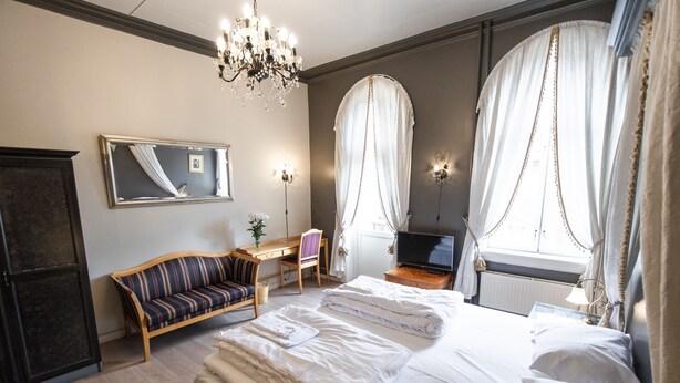 A hotel room with a large bed, a desk, a chair, a television, and a mirror.