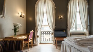 Ein Hotelzimmer mit Bett, Schreibtisch mit Stuhl, Fernseher und einem Fenster mit Vorhängen.