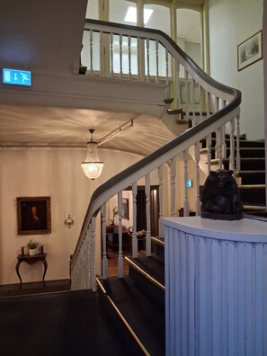 A grand staircase with a chandelier, a framed portrait, and a statue on a pedestal. - Grand Hotel Hønefoss (Ringerike)
