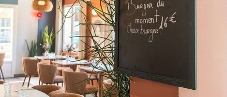 Interior d'un restaurant amb un quadre negre que mostra articles com 'Tarte de Boeuf' i 'Burger du moment'.