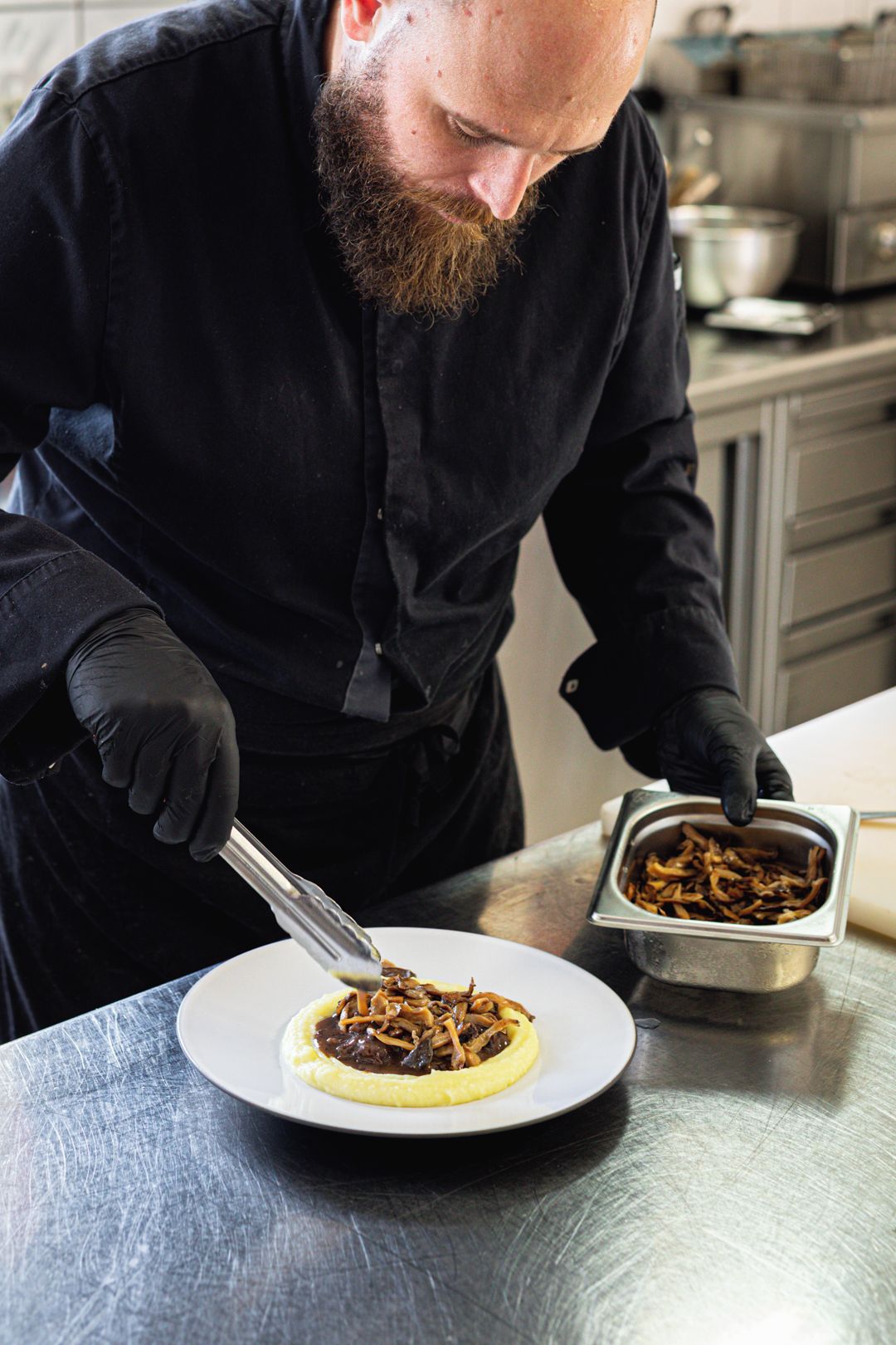 A person in a black shirt and gloves preparing food on a stainless steel table.