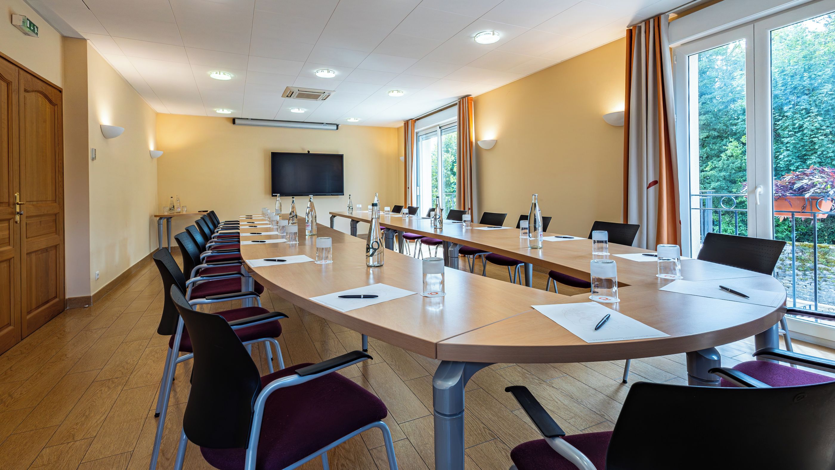 A conference room with a long table, chairs, and a television screen.