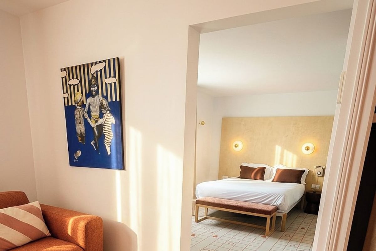 A hotel room with a bed, a bench, a sofa, and a painting on the wall.