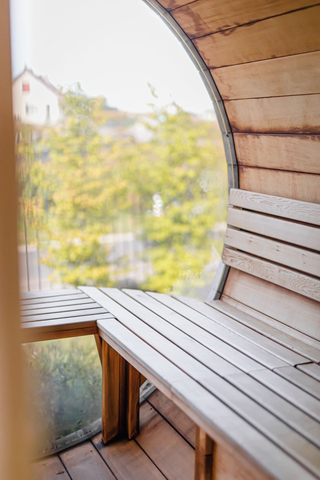 Un banco de madera con vistas a zonas verdes y un edificio, todo visible a través de un ventanal circular.