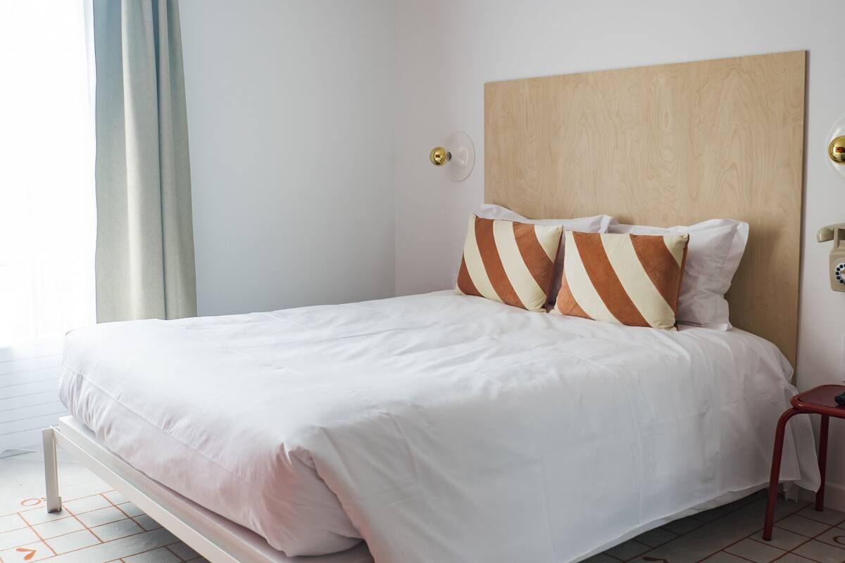 A modern hotel room with a single bed, a wooden headboard, and a patterned floor.