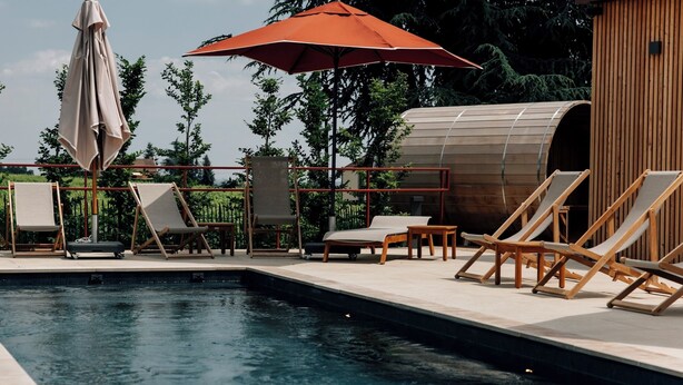 A pool area with lounge chairs and a wooden structure, likely a sauna or steam room, in a landscaped setting.