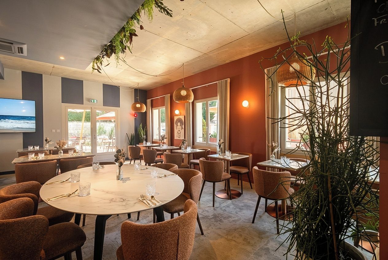 Un restaurante con mesas redondas, sillas, luces colgantes y una gran pantalla de televisión.