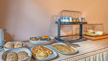 A breakfast buffet with various breads, pastries, and a coffee station.