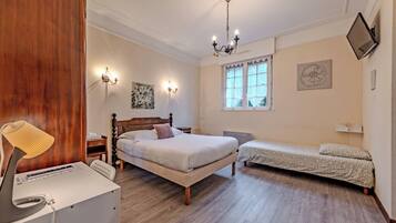 A bedroom with a wooden bed, a bedside table, a lamp, a radiator, a window, and artwork on the wall.