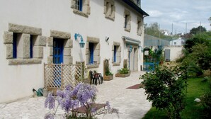 A stone-paved courtyard with a white building featuring blue-framed windows and doors. There is a potted plant with purple flowers in the foreground. - Hotel De la Corniche (Brest)