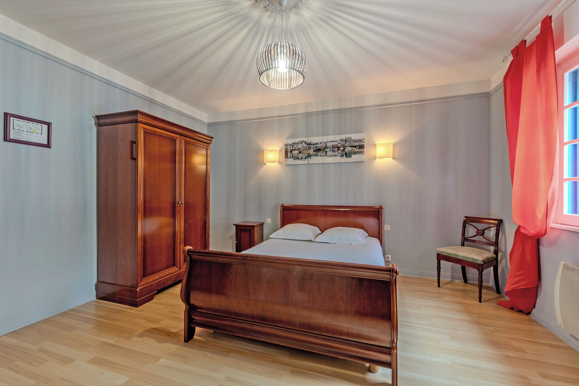 A bedroom with a wooden bed, a wardrobe, a chair, and a picture on the wall.