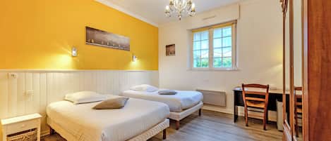 A room with two beds, a desk, a chair, a chandelier, and a window.