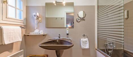 A bathroom with a large sink, a mirror, a towel rack, a shower, and a window.