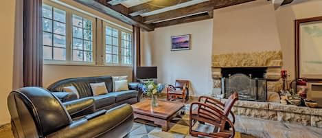A living room with a fireplace, leather sofa, wooden chairs, and a large window.