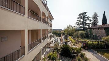 Un edificio de varios pisos con balcones, un patio con plantas y una vista de árboles y edificios a lo lejos.
