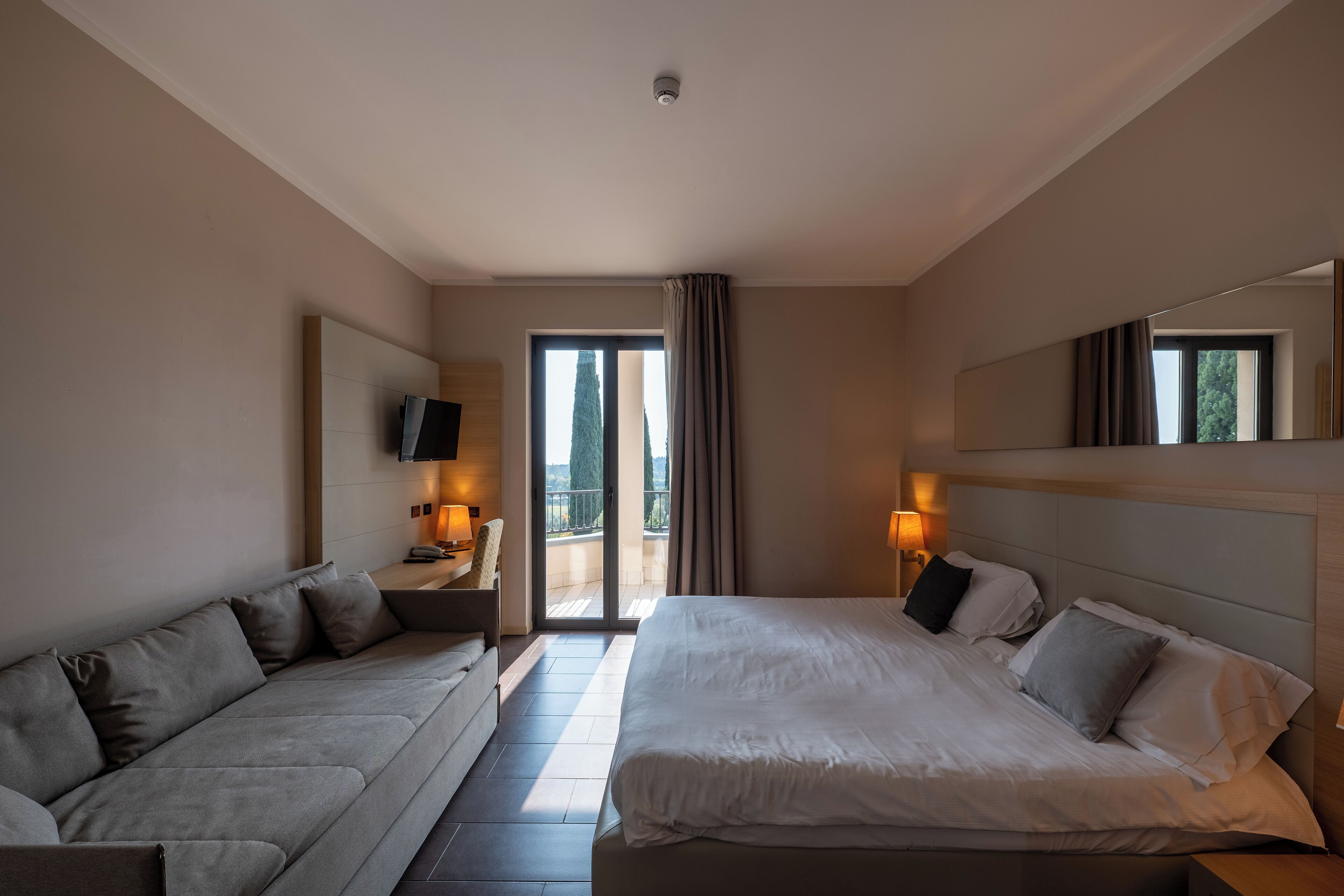 Een hotelkamer met een bed, een slaapbank, een televisie en een balkon met gordijnen.