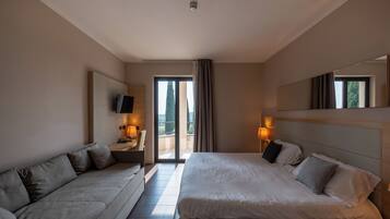 Een hotelkamer met een bed, een slaapbank, een televisie en een balkon met gordijnen.