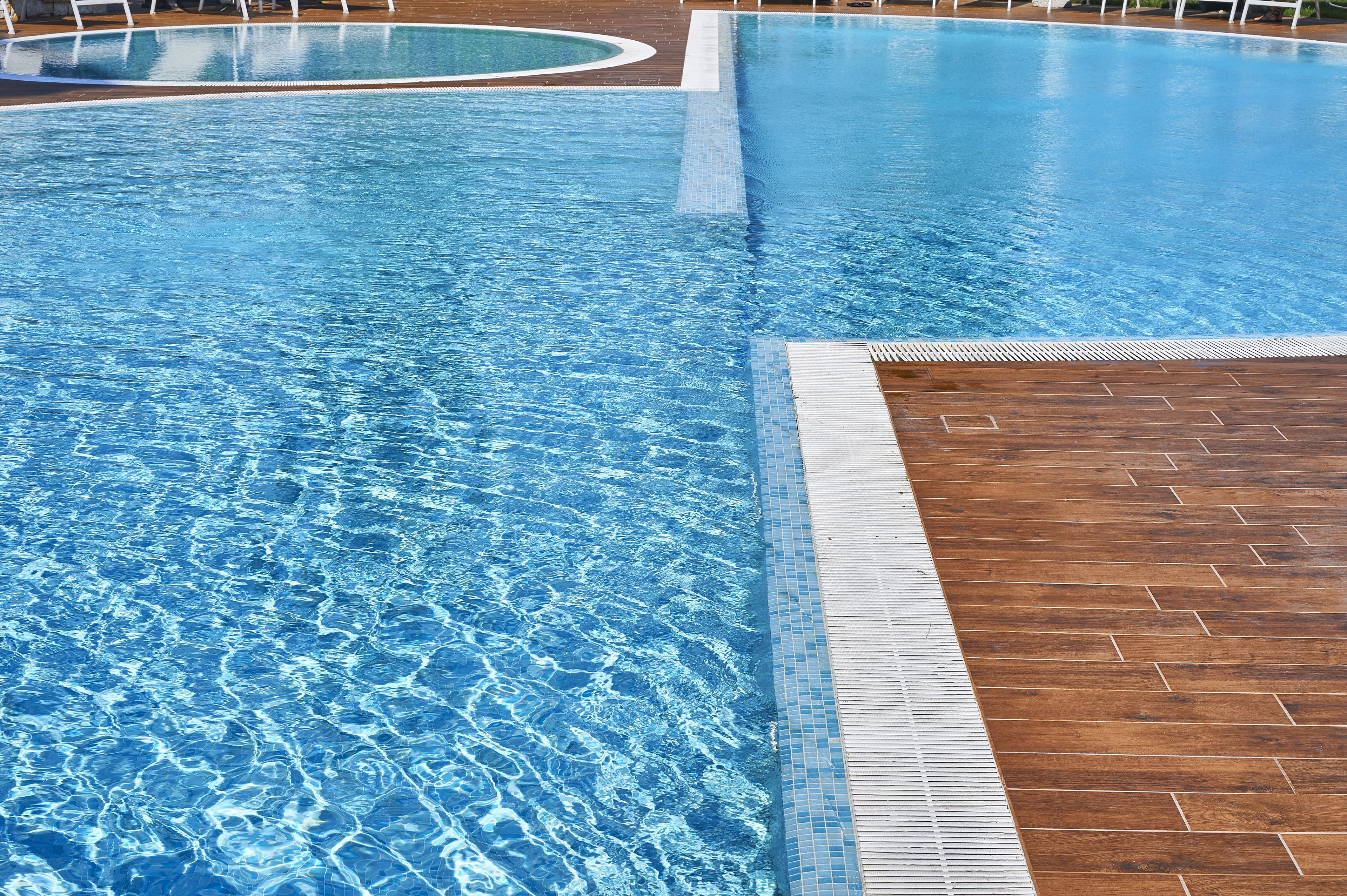 A large, clear swimming pool with a wooden deck area.