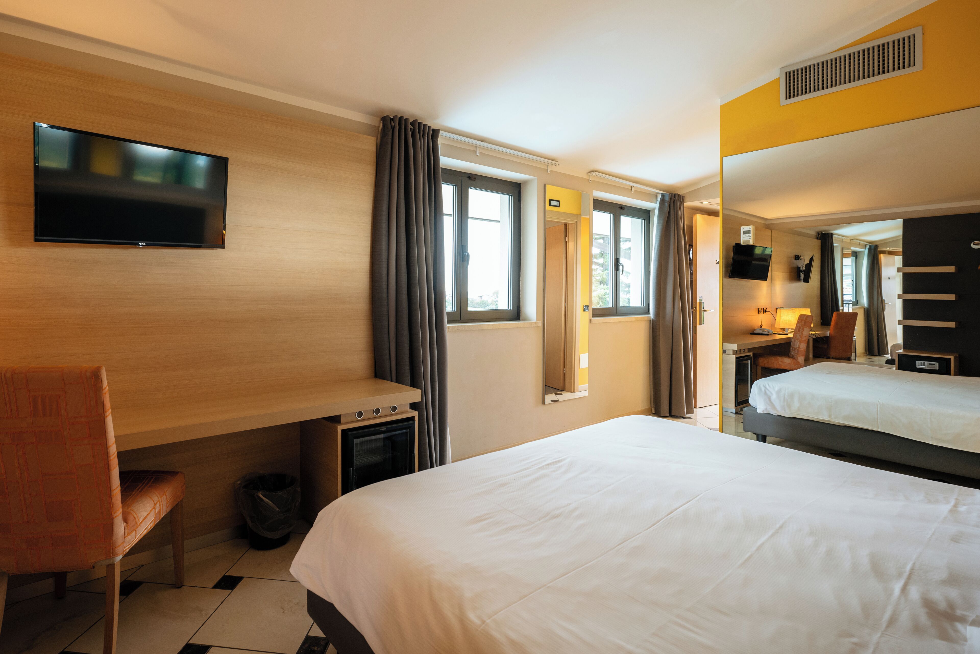Une chambre d’hôtel avec un lit, un bureau, une chaise, une télévision et une fenêtre avec des rideaux.