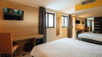 A hotel room with a bed, a desk, a chair, a TV, and a window with curtains.