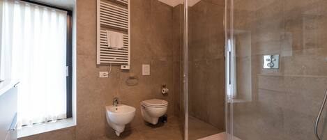 A modern bathroom with a glass shower enclosure, a bidet, and a toilet.