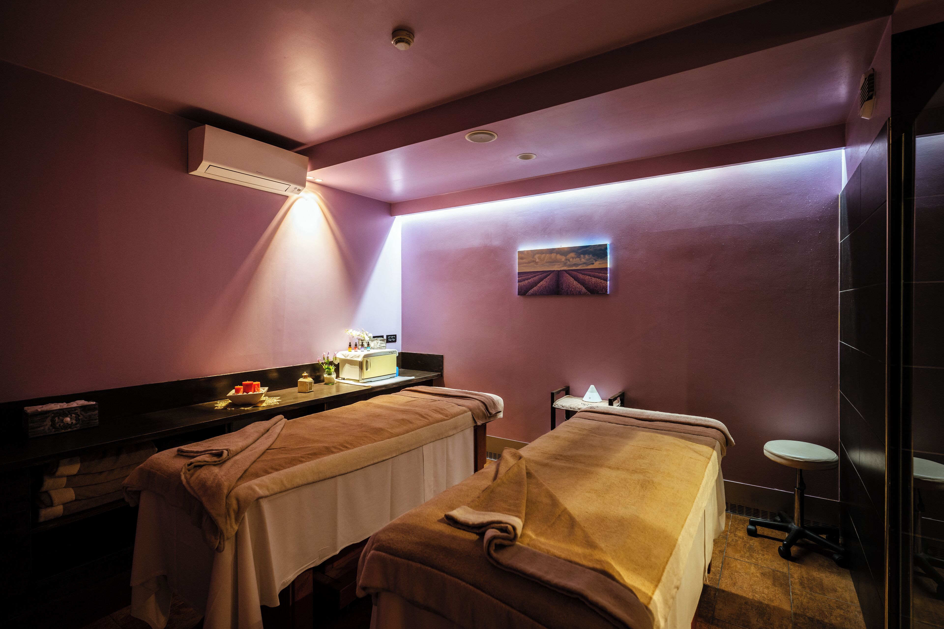 Ein Spa-Raum mit zwei Massagetischen, einem kleinen Tisch mit Lampe und einer wandmontierten Klimaanlage.