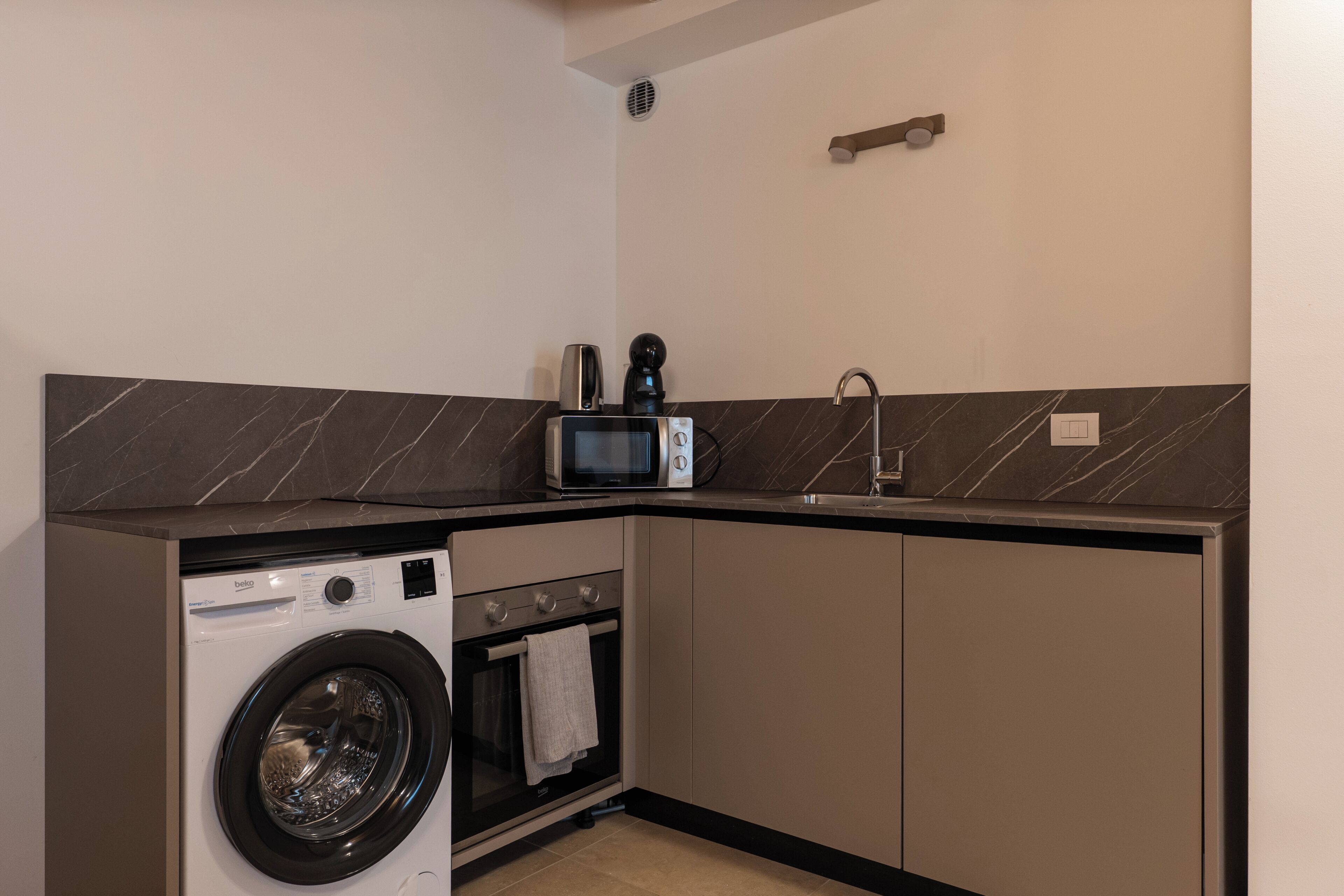 Cocina compacta con lavadora, microondas y un lavamanos pequeño.