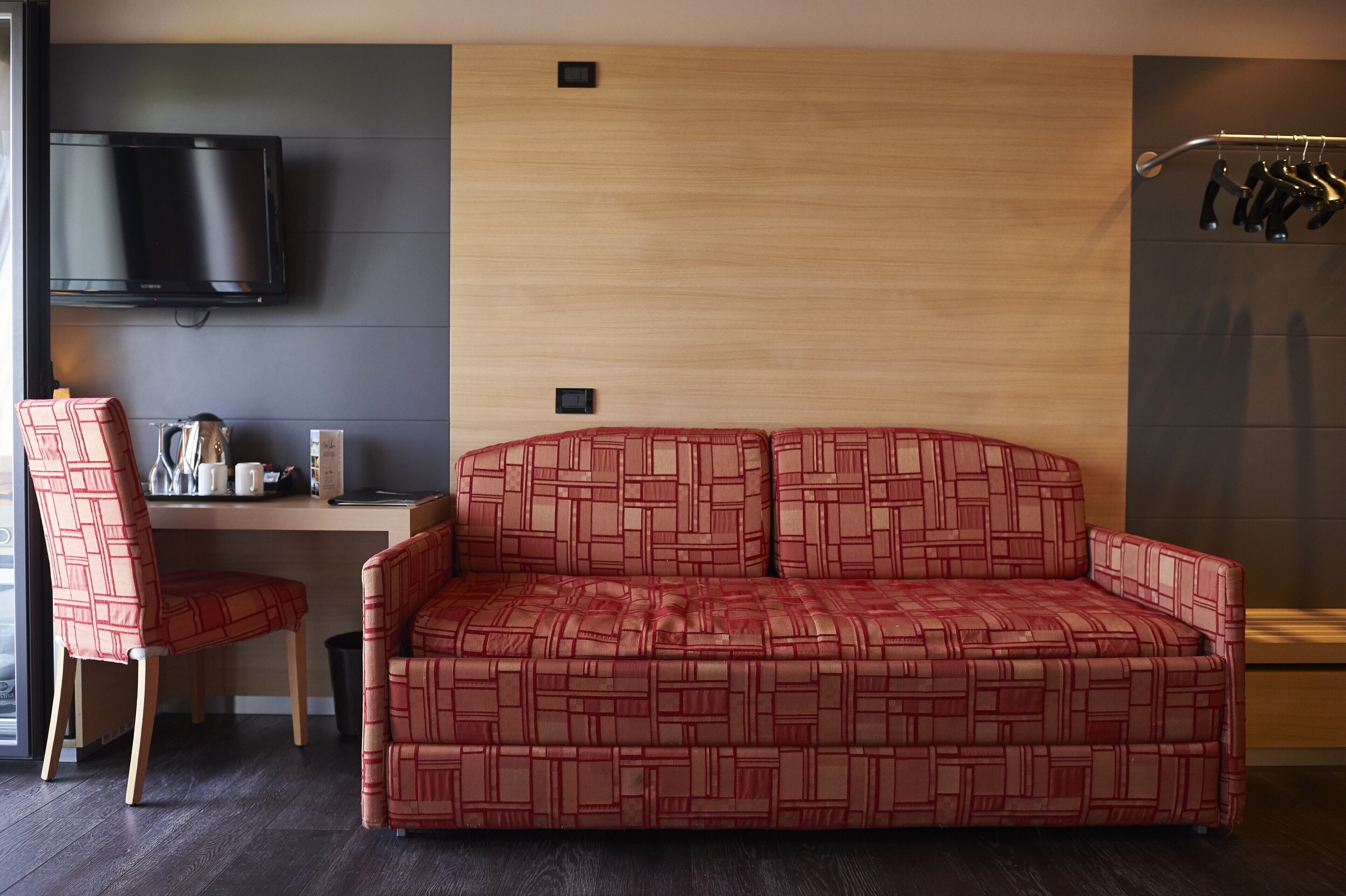 Una habitación moderna con sofá, escritorio, silla, televisor y perchero.