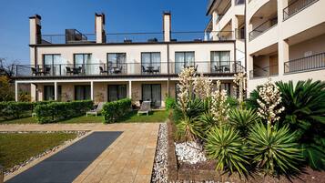 A modern hotel with a covered outdoor seating area, a swimming pool, and landscaped gardens.