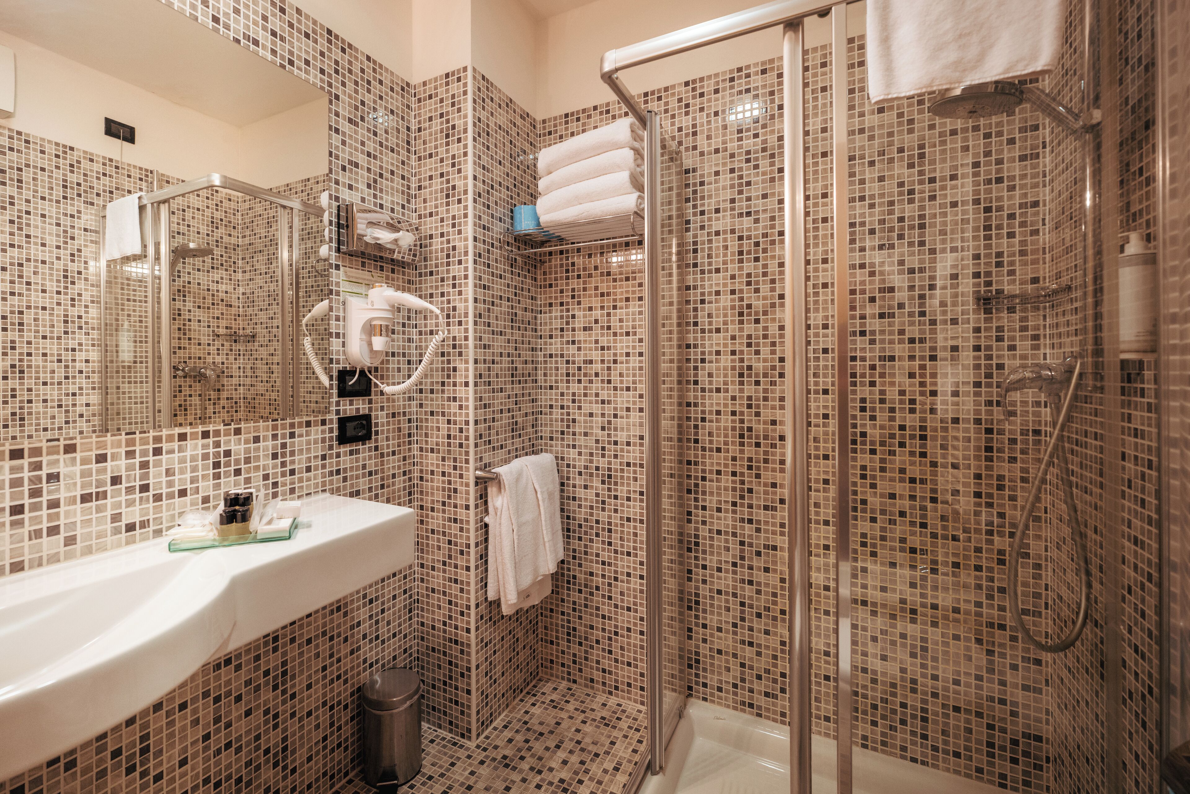 A bathroom with a glass-enclosed shower, a white sink, and a tiled mosaic wall.