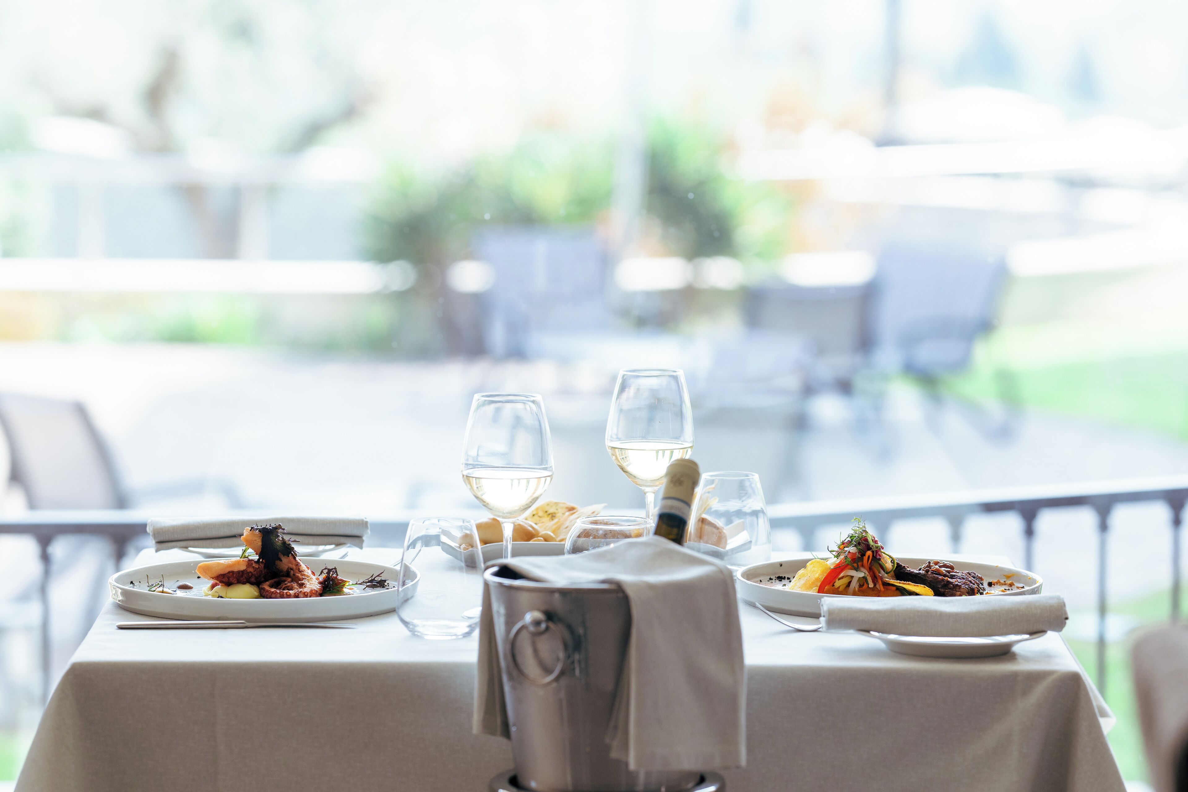 Una mesa de comedor dispuesta con platos de comida, copas de vino y una jarra de metal.