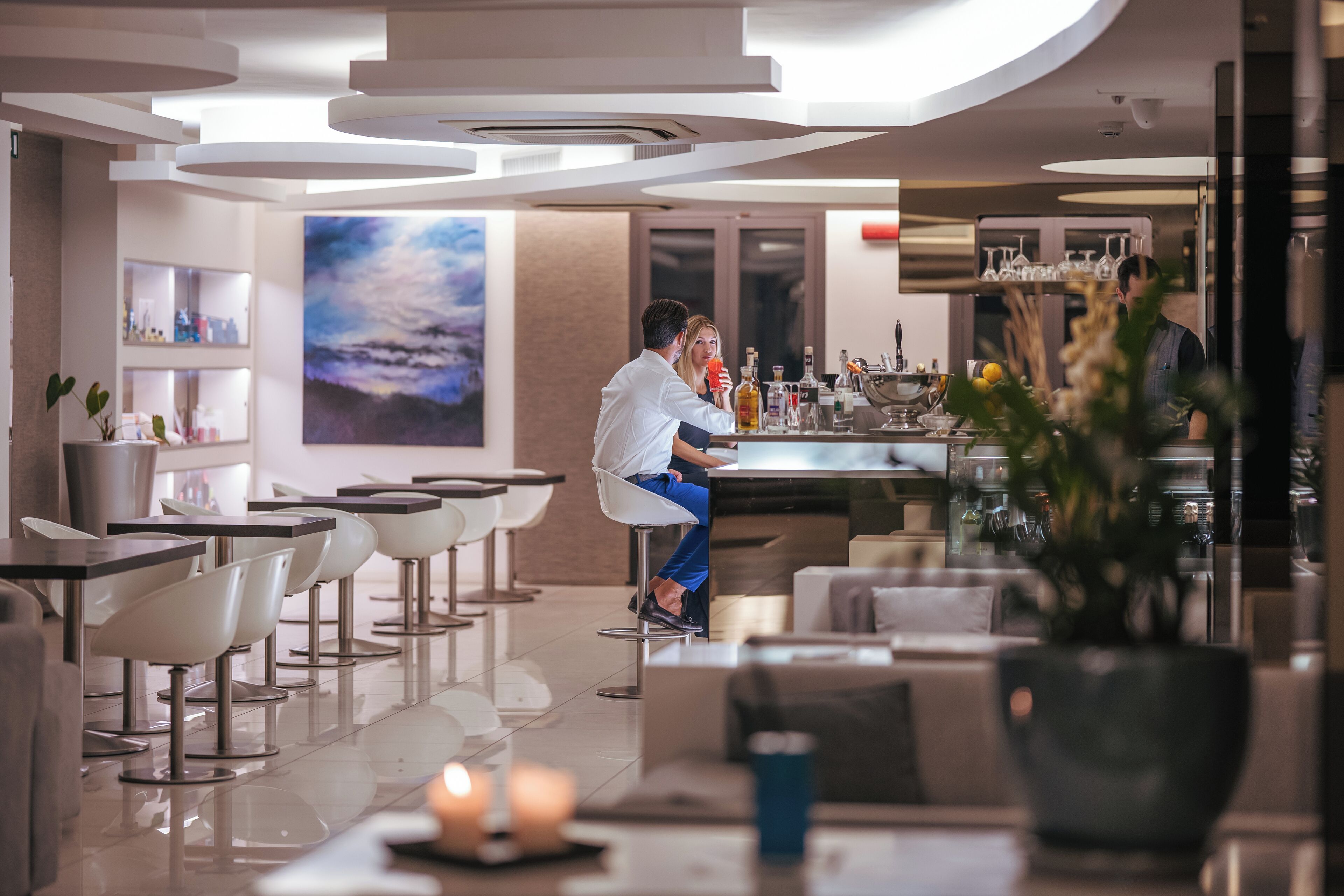 Un espace bar moderne, doté d’un comptoir, de sièges et d’un grand tableau mural.