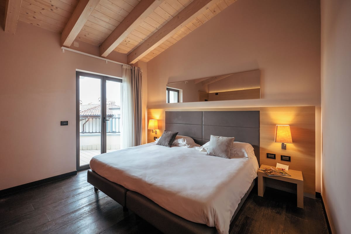 Habitación de hotel con una cama grande, dos lámparas de noche, techo de madera y vistas a través de una puerta de cristal.