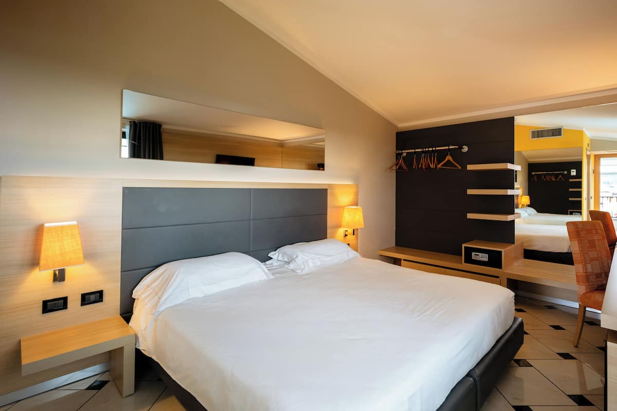 Una habitación de hotel moderna con una cama grande, mesitas de noche con lámparas, un espejo y un armario con perchero.