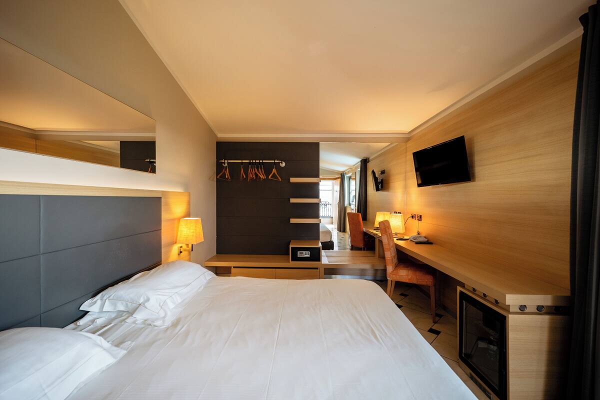 Una habitación de hotel moderna con una cama grande, un escritorio, un televisor de pantalla plana y una zona de estar con una mesa y sillas.