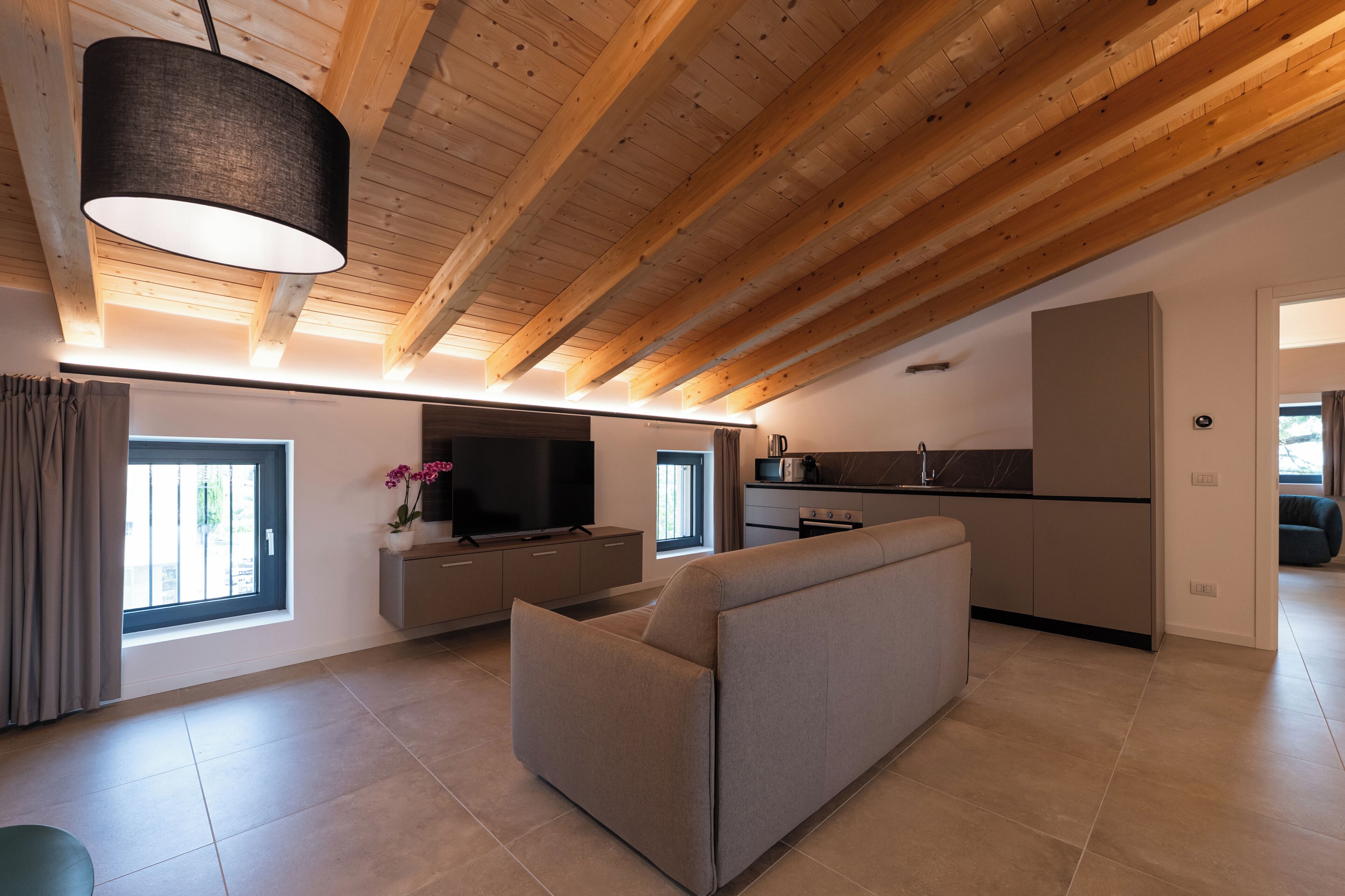 Un interior moderno con sofá, televisión, cocina y vigas de madera en el techo.
