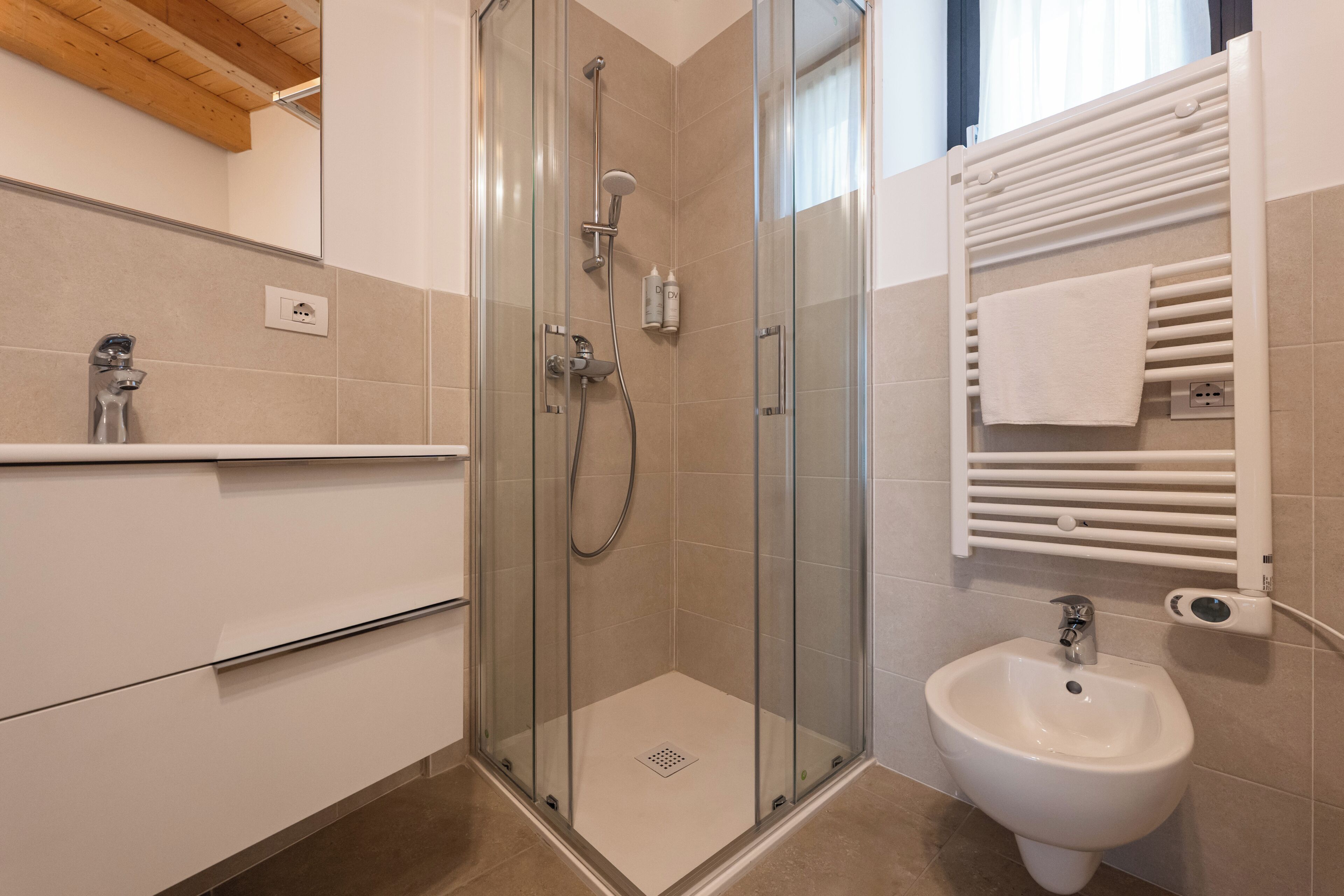 A modern bathroom with a glass-enclosed shower, a white pedestal sink, and a towel rack.