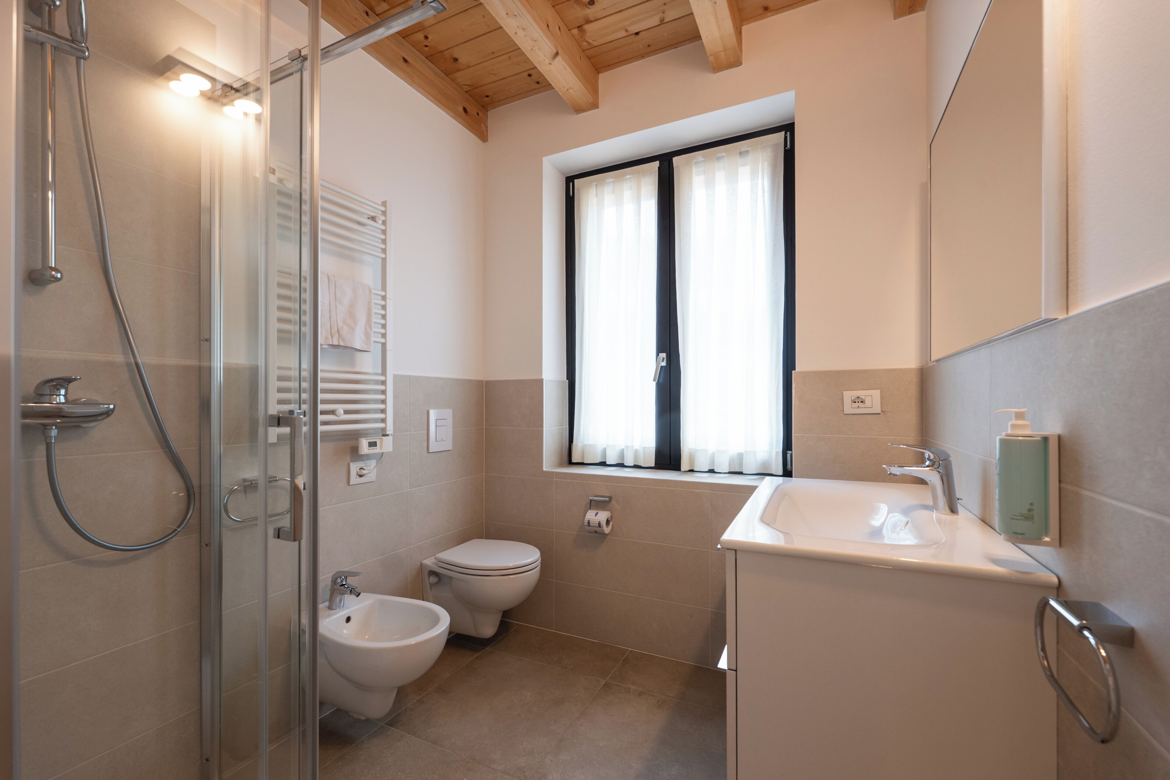 A modern bathroom with a glass-enclosed shower, a bidet, a toilet, and a sink with a mirror above.