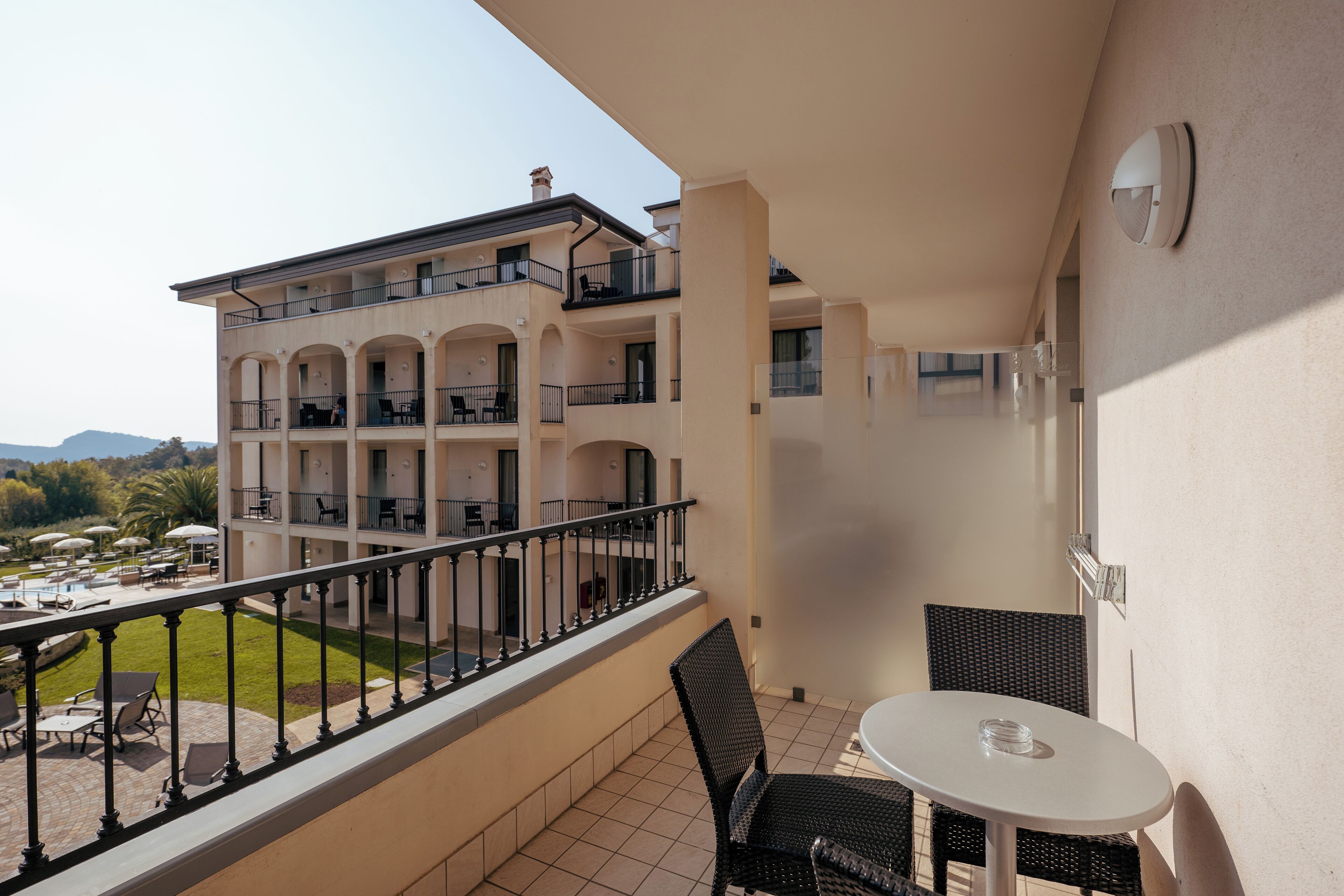 A balcony with a table and chairs, overlooking a pool and a building with multiple balconies.