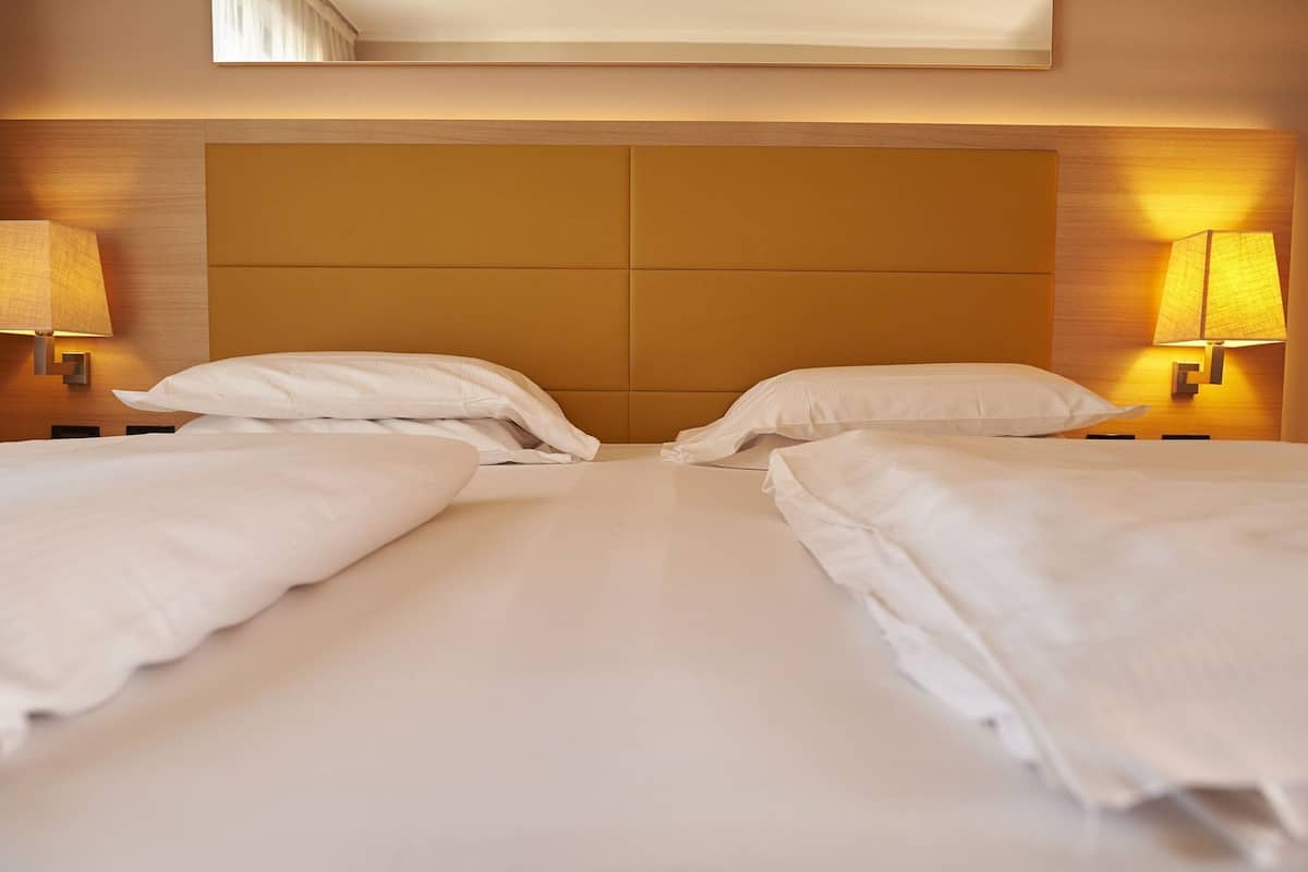 Una habitación de hotel con una cama doble, dos lámparas de noche y un cabecero.