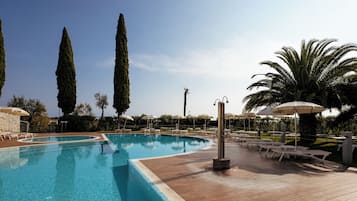 Una piscina con lettini e ombrelloni, circondata da alberi alti e palme.