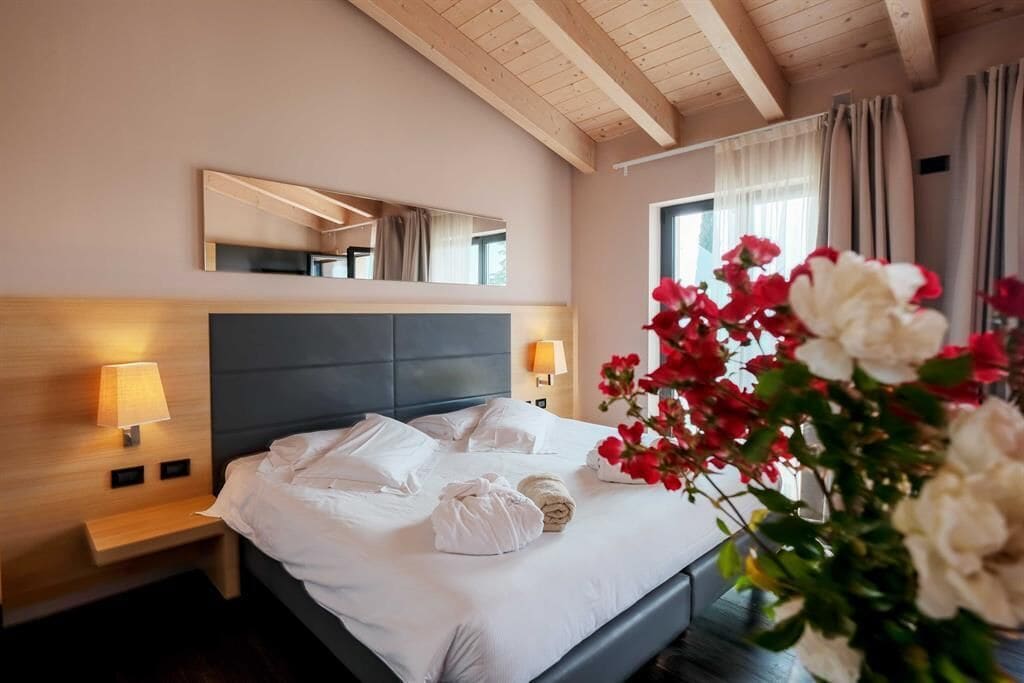 Una habitación de hotel con cama, lámparas de noche, un espejo y una ventana con cortinas.
