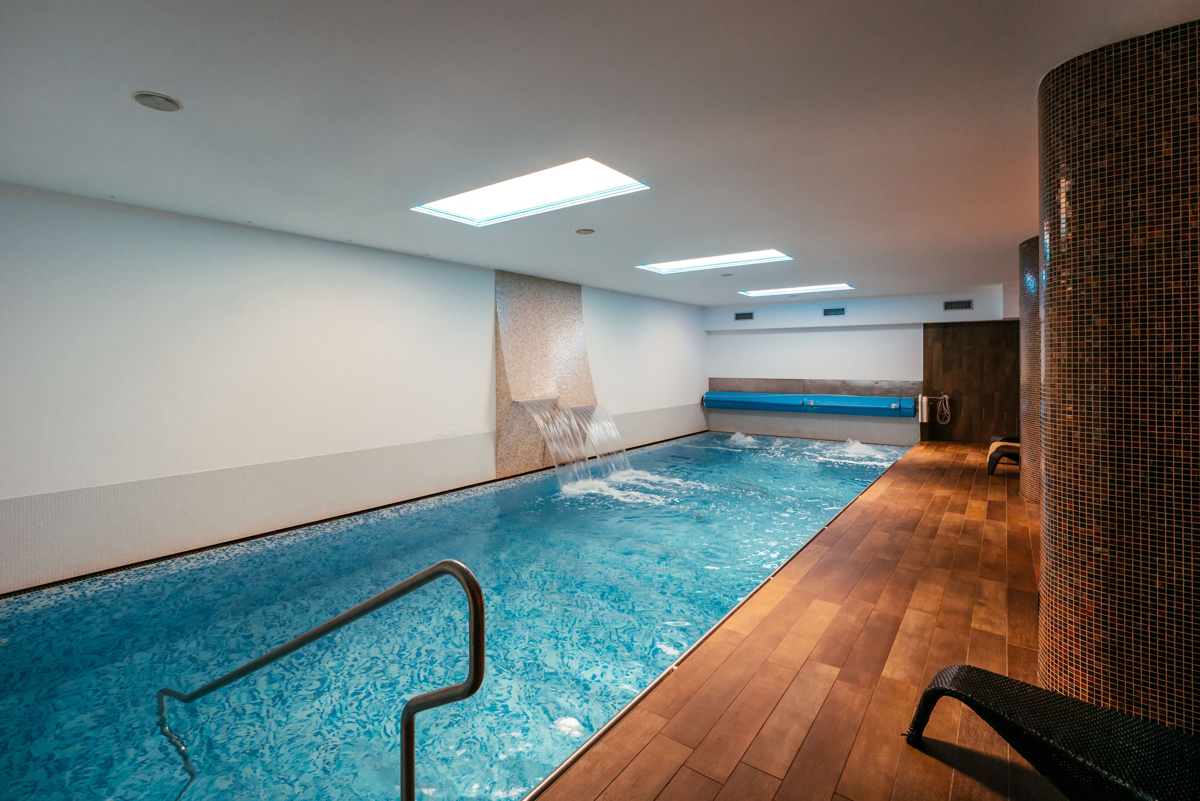 An indoor swimming pool with clear water, wooden flooring, and a bench along the wall.