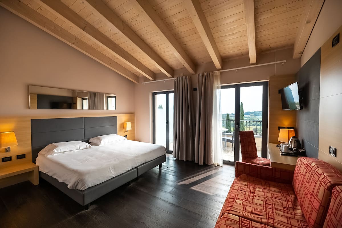 Habitación de hotel con una cama grande, un sofá, un televisor y un balcón con cortinas.