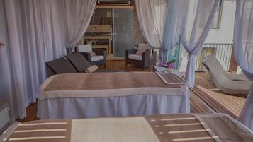 Ein Zimmer mit einem Bett, zwei Stühlen, einem kleinen Tisch und einem Balkon mit Geländer.