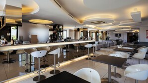 Een moderne bar met een lange toonbank, witte barkrukken en diverse zitplaatsen, waaronder banken en hoge tafels.