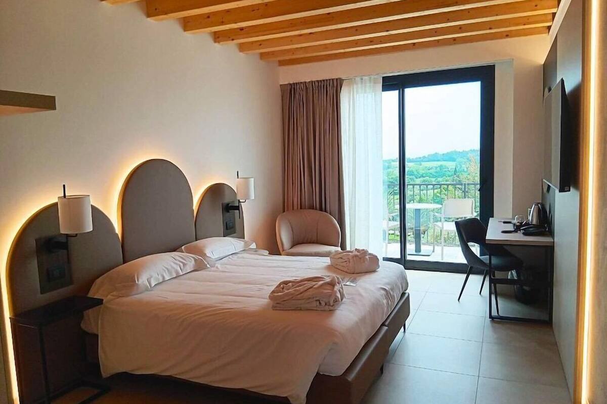 Habitación de hotel con cama, escritorio, silla, televisor y balcón con vistas.