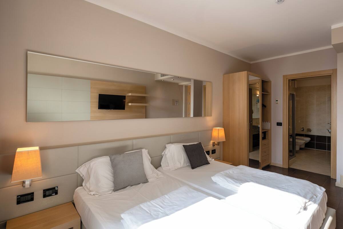 Habitación de hotel con dos camas, un espejo grande, televisión y baño visible a través de una puerta abierta.