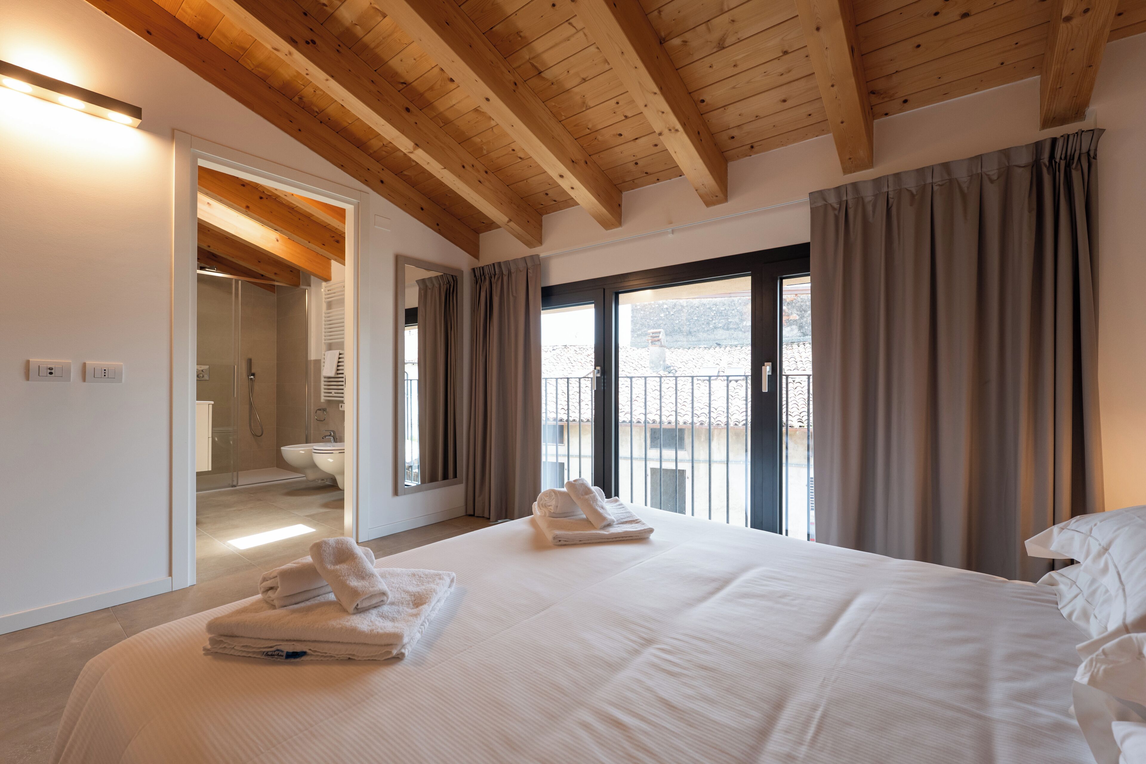 A hotel room with a large bed, a bathroom, and a balcony with curtains.