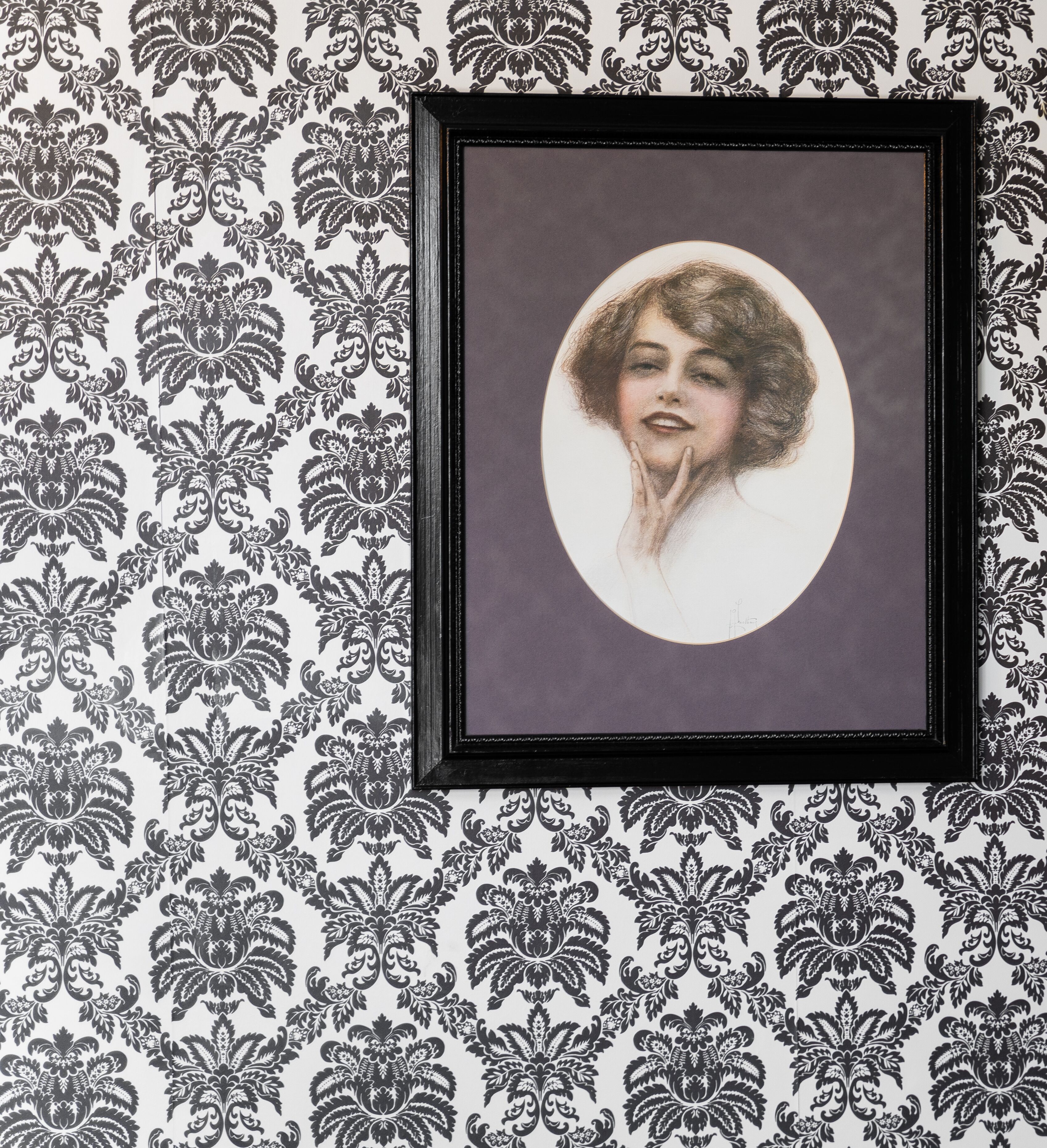 A framed portrait with a circular background, set against a patterned wallpaper.